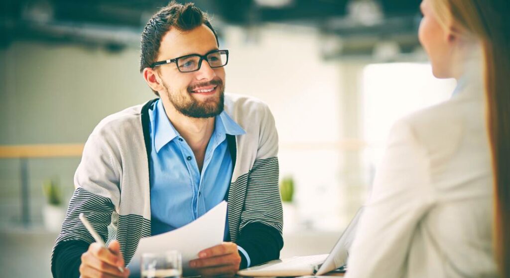 Smiling man in glasses discussing marketing strategies with a woman in a business setting, illustrating collaboration in digital marketing services at Block 24 Marketing.