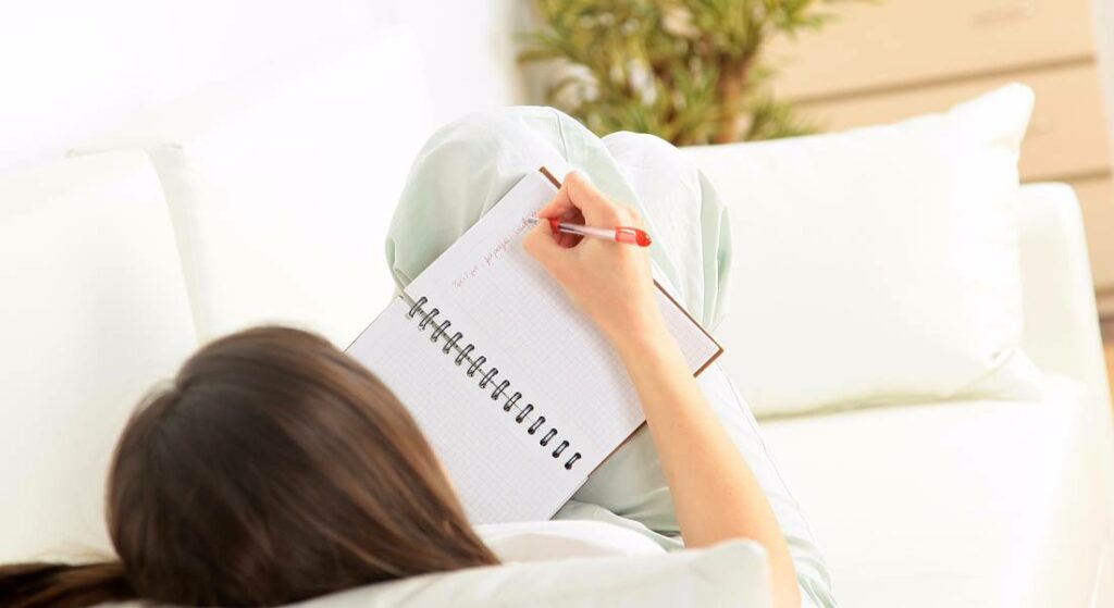 Person writing in notebook while relaxing on a couch, symbolizing creativity and idea generation in digital marketing.