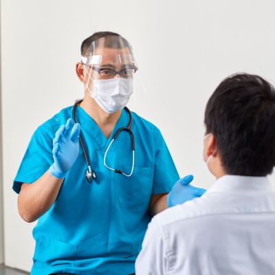 Healthcare professional in blue scrubs and face shield consulting with a patient, emphasizing trust and patient engagement in healthcare settings.