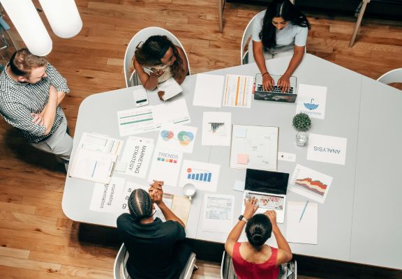 Group of diverse professionals collaborating at a table, analyzing charts and reports related to digital marketing strategies and SEO performance.