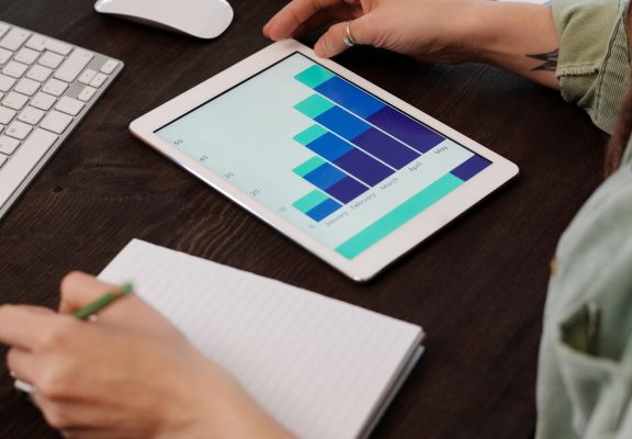 Person analyzing data on a tablet with a bar graph, notebook, and pencil, illustrating digital marketing performance and SEO metrics.