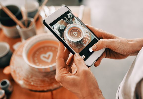 Person taking a photo of a beautifully crafted bowl with a heart design, surrounded by art supplies, illustrating engagement in creative content creation.
