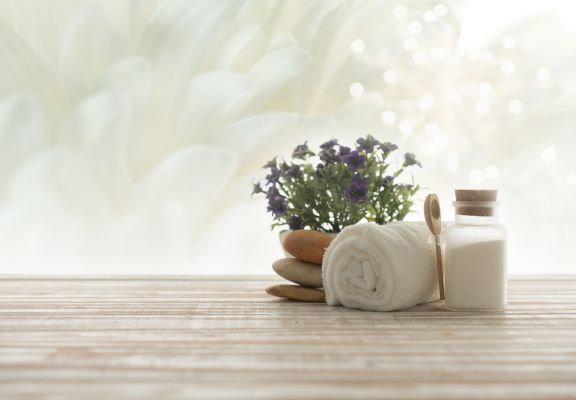 Spa setting with rolled white towel, smooth stones, small vase of purple flowers, and glass jar, evoking relaxation and beauty treatments for medical spas.
