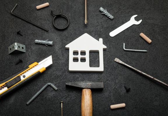 House-shaped icon surrounded by various tools like a hammer, utility knife, and screws, symbolizing home services and maintenance.