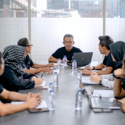 Group of diverse professionals engaged in a coaching strategy meeting, discussing digital marketing and lead generation for coaching brands, with a laptop and water bottles on the table.