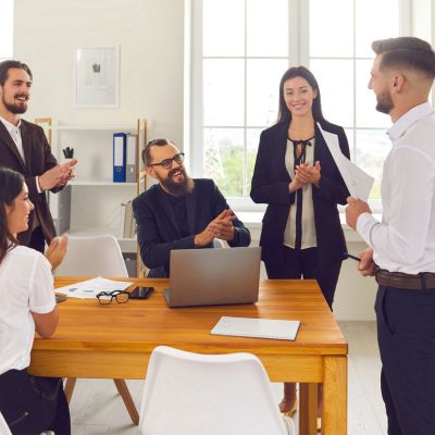 Group of professionals in a modern office celebrating a presentation, emphasizing teamwork and client engagement in coaching business strategies.