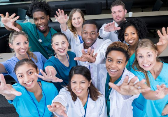 Diverse group of healthcare professionals smiling and reaching out, representing patient-focused care and community engagement in healthcare marketing.