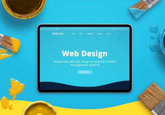 Tablet displaying a vibrant web design homepage with a blue background, surrounded by paintbrushes and colorful paint, symbolizing modern and responsive web design services.